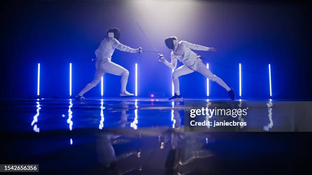 due schermitori professionisti sventano spade duellando l'un l'altro in combattimento con un'epica illuminazione blu del palcoscenico. parare un colpo - fioretto sport foto e immagini stock