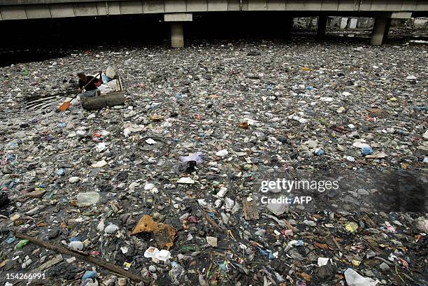 An Indonesian man on a boat salvages scrap items in a river choked with trash in Surabaya city in East Java province on October 17, 2012. AFP PHOTO /...