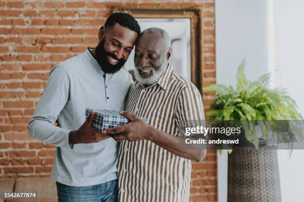 adult son giving gift to senior father - father gift stock pictures, royalty-free photos & images