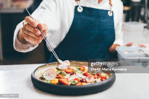 close up a chef preparing a gourmet dish. chef is decorating the plate just before the serving. - uniforme de chef fotografías e imágenes de stock