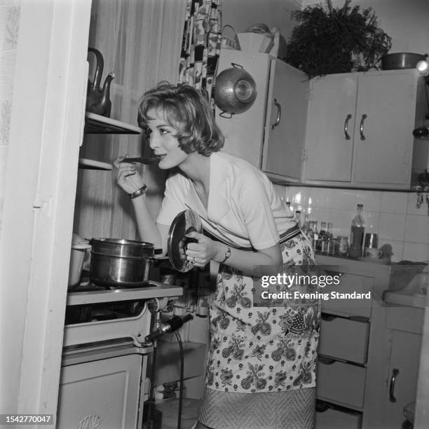 British model Sandra Paul leaning over a saucepan to taste the food she is cooking, April 23rd 1959.