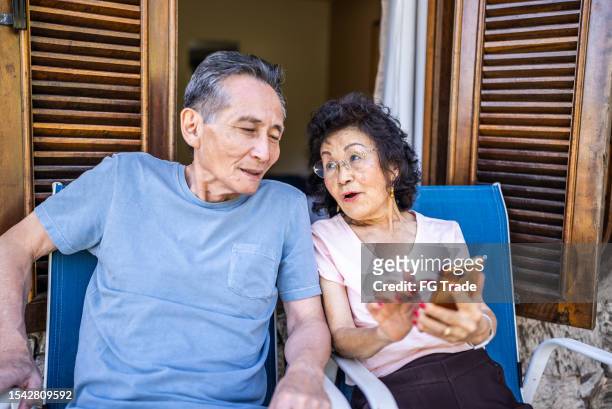 senior woman showing something on mobile phone to her husband on hotel balcony - real wife sharing 個照片及圖片檔