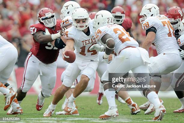 Quarterback David Ash of the Texas Longhorns hands off during a game in front of defensive tackle Jamarkus McFarland of the Oklahoma Sooners on...