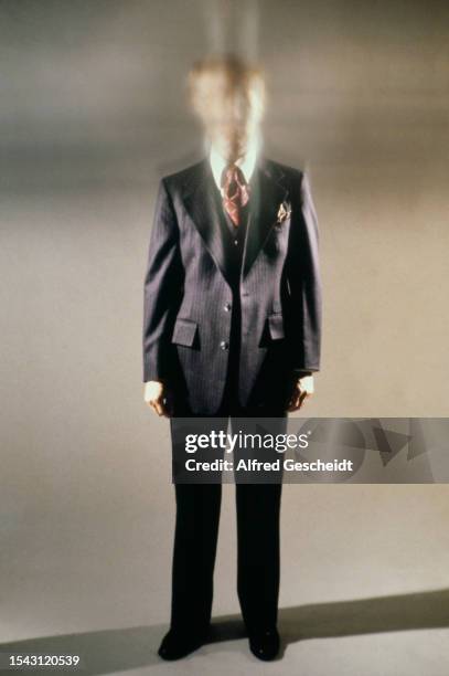 Full-length image of a man in a three-piece pinstripe suit, with a white shirt and a red-and-white tie, his face obscured by blurring, against a...