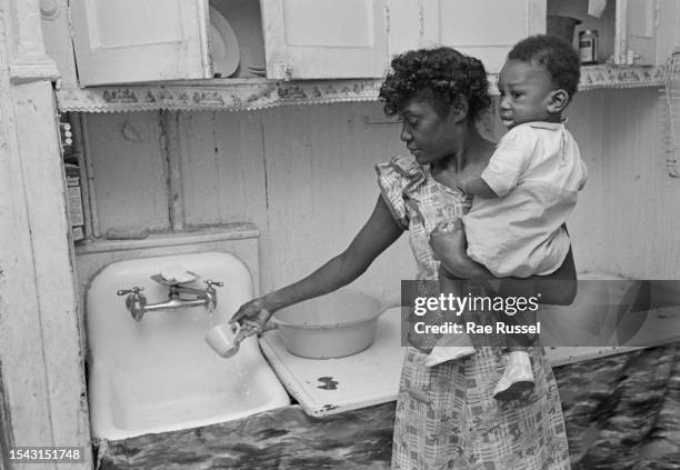 Woman holding a young child rinses a cup under a tap over a sink in a property at a social housing development on Henry Street in the Lower East Side...