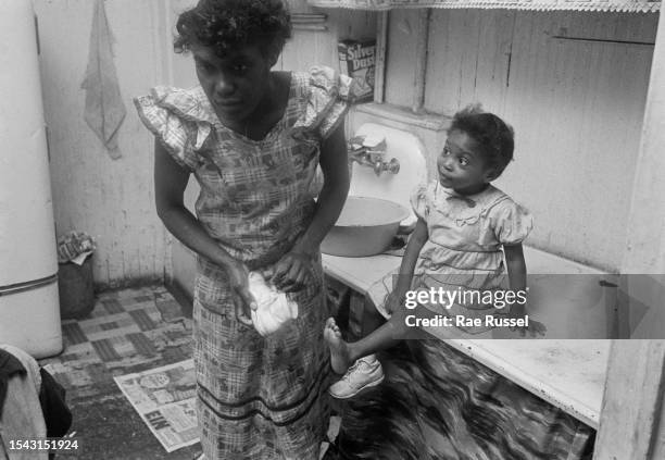 Woman helping her daughter, who sits on the counter, with her leg stretched out in anticipation of her shoe, which is held by her mother, in a...