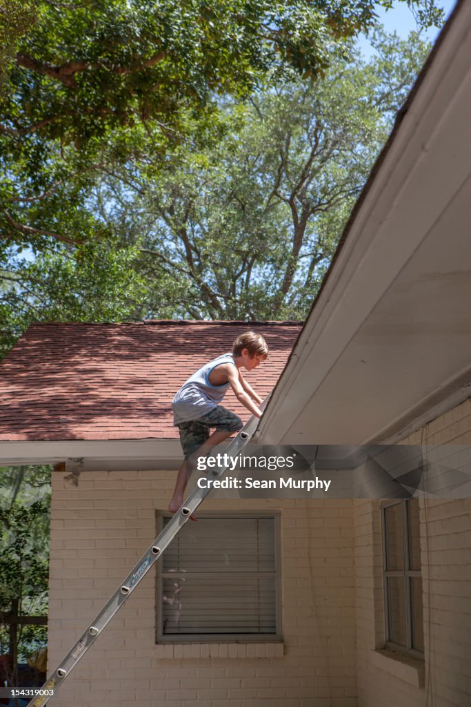 Young boy climbing a latter onto a roof