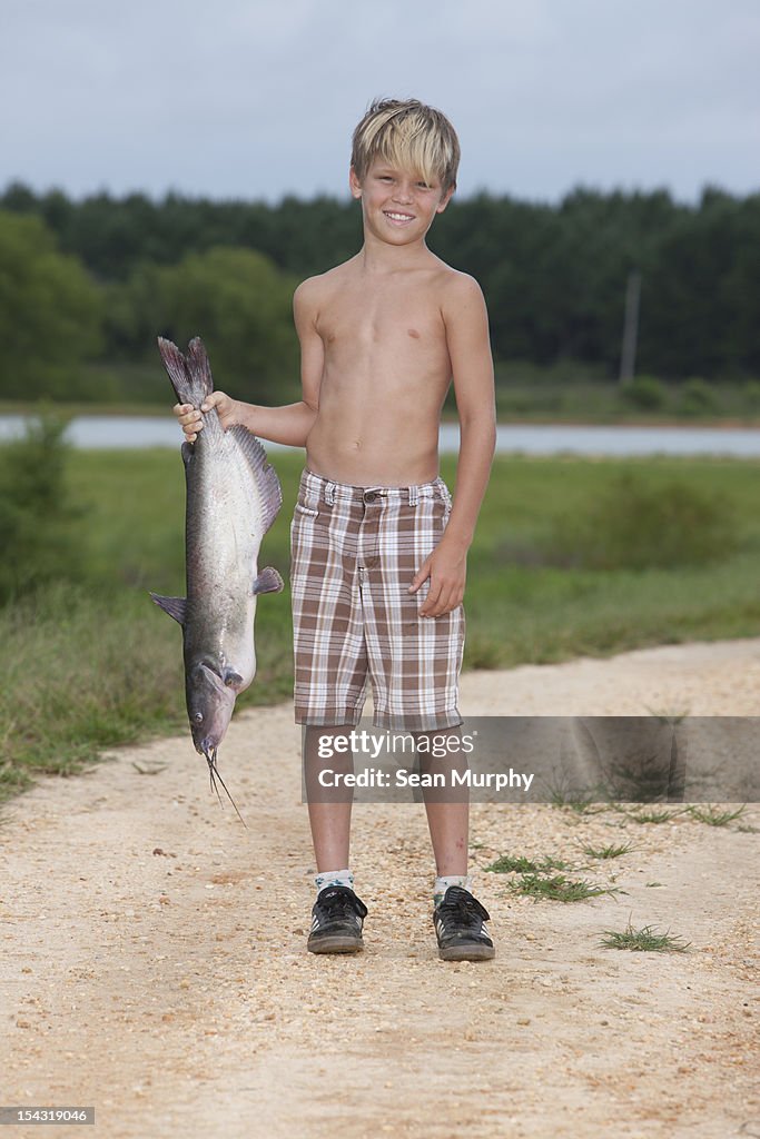 Young Boy Holding a Fish Next to River