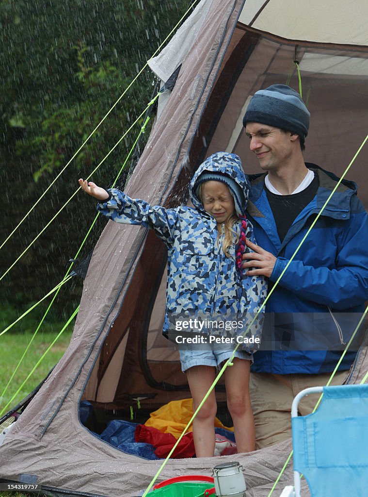 Father and daughter testing rain from inside tent