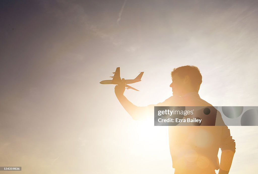 Man holding a model plane against sunset.