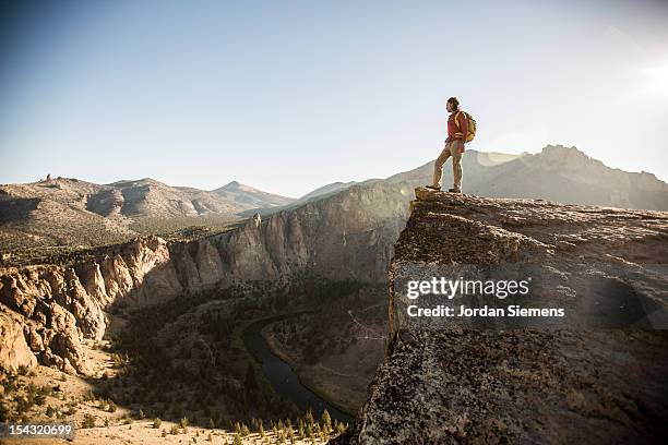 a man standing on top of a tall cliff. - smith rock state park fotografías e imágenes de stock