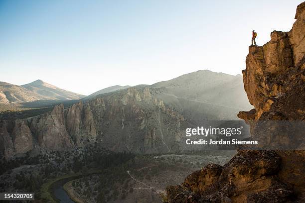 a man standing on top of a tall cliff. - ledge stock pictures, royalty-free photos & images
