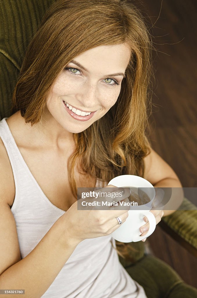 Smiling young woman drinking tea in armchair