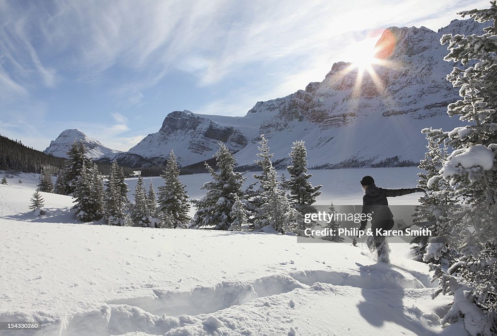 Canada, Alberta, Banff National Park, Woman snowshoeing through deep snow by mountain lake