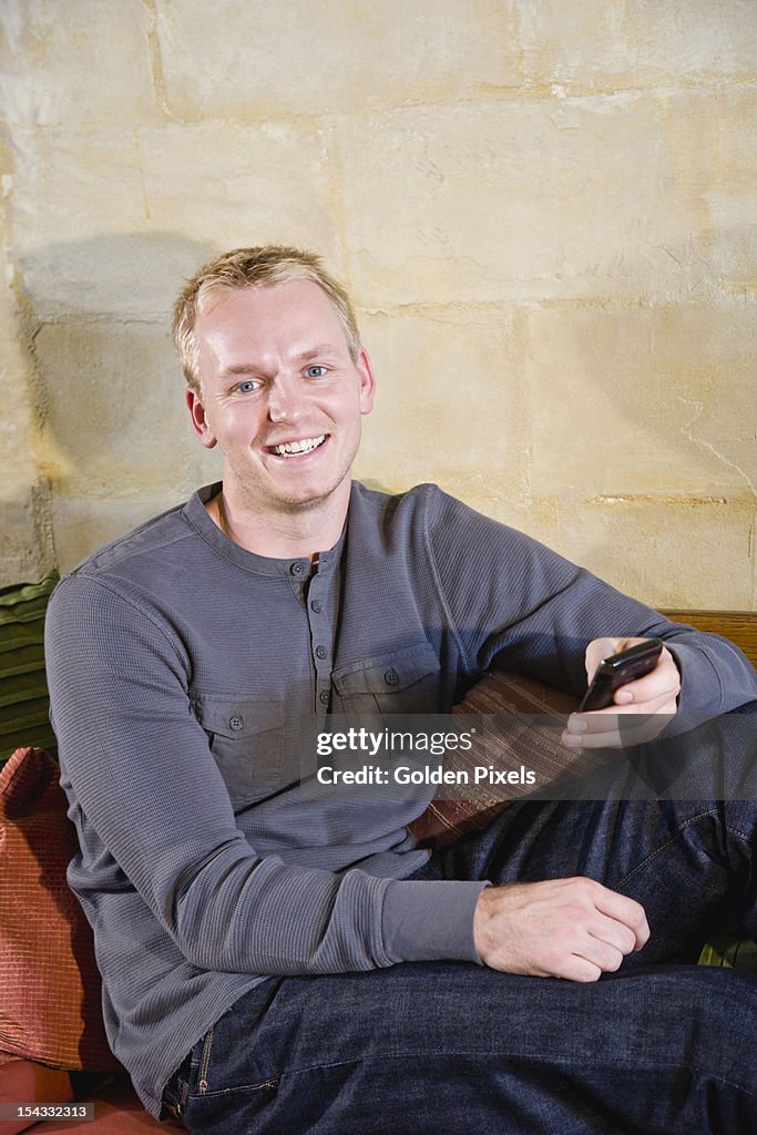 Man relaxing on sofa texting on mobile phone