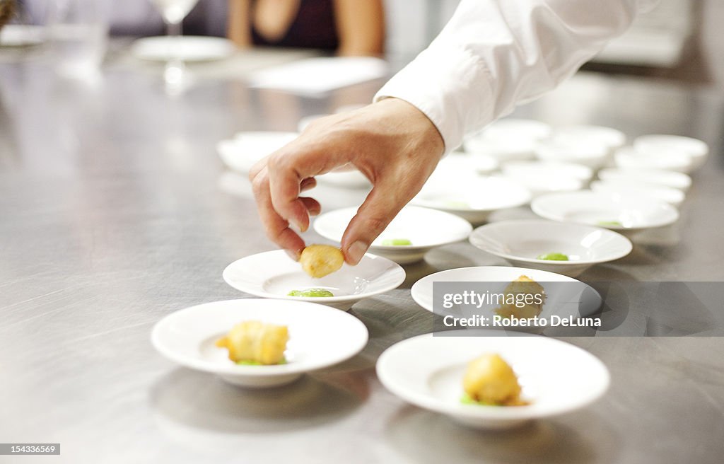 USA, New York City, Brooklyn, close up of chef's hand putting appetizers on plates