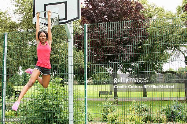 woman hanging from basketball net - natural shot female stock-fotos und bilder