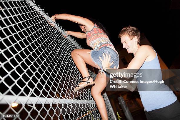 man helping girlfriend climb fence - man climbing fence stock pictures, royalty-free photos & images
