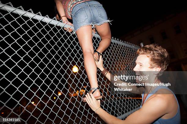 man helping girlfriend climb fence - friend mischief stock pictures, royalty-free photos & images