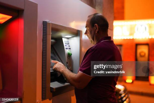 senior man makes deposits at atm in the evening - decal stock pictures, royalty-free photos & images