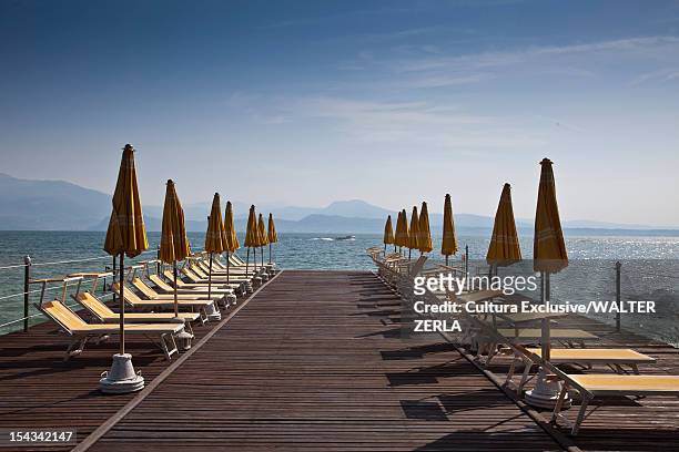 lawn chairs and umbrellas on wooden deck - sirmione stock pictures, royalty-free photos & images
