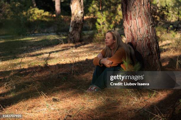 beautiful sad mature woman leaning against tree in forest. emotional burnout. - autumn sadness stock pictures, royalty-free photos & images