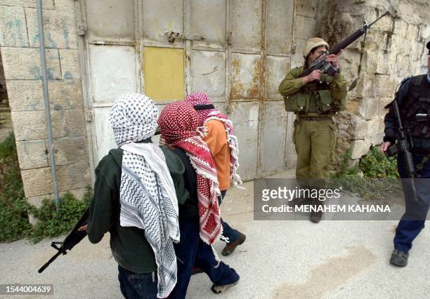 An Israeli soldier stands guard as children of Jewish settlers dressed up as Palestinians celebrate Purim 07 March 2004 in the divided West Bank city...