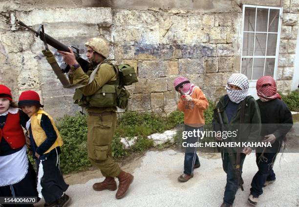 An Israeli soldier patrols as children of Jewish settlers dressed up as masked Palestinian militants take part in the Purim celebrations 07 March...