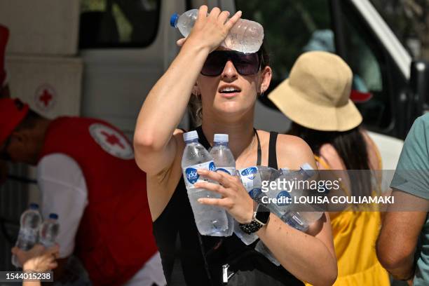 Woman cools off with cold bottles of water, distributed by the hellenic red cross organization near the entrance of the Acropolis archeological site...