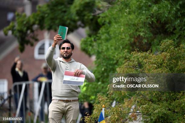 Protestor Salwan Momika holds up the Muslim holy book and a sheet of paper showing the flag of Iraq during a protest outside the Iraqi Embassy in...