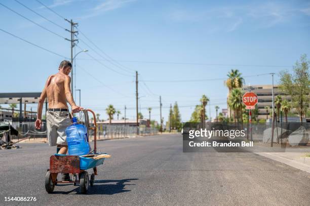 Person transports water jugs through a neighborhood on July 14, 2023 in Phoenix, Arizona. Today marks the Phoenix area's 15th consecutive day of...