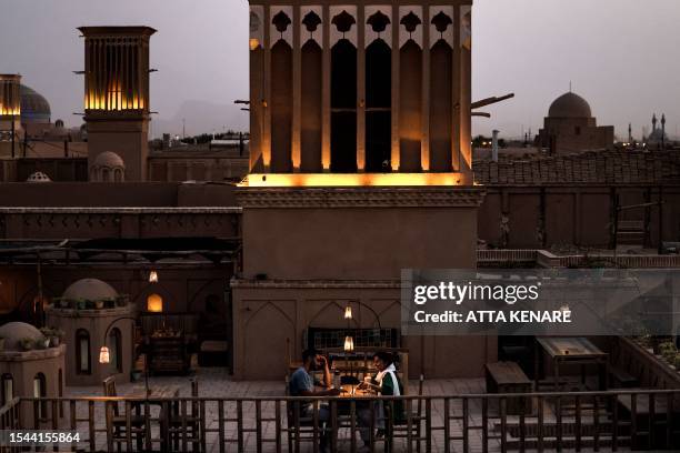 Couple sit for drinks by a wind-catcher at a rooftop cafe in Iran's central city of Yazd on July 3, 2023. Tall, chimney-like towers rise from...