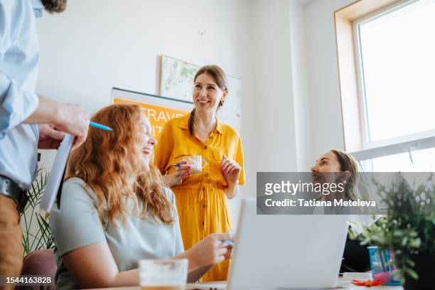 smiling office managers are results oriented, using laptop and laughing with customers in bright office - creative agency stock pictures, royalty-free photos & images