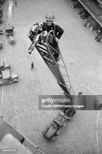 Men Of The Auxiliary Fire Service In London, C 1940, A member of the Auxiliary Fire Service stands at the top of a partly-extended turntable ladder...