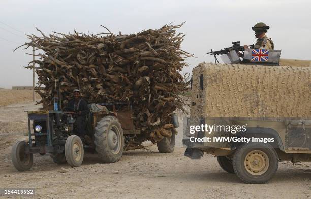 British Forces In Afghanistan 2006 - 2007, A local civilian driving a tractor loaded with wood passes an Army landrover during the first British Army...