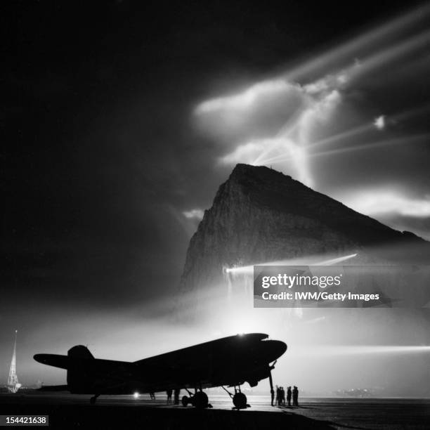 Douglas Dakota of BOAC, silhouetted by night at Gibraltar by the batteries of searchlights on the Rock, as it is prepared for a flight to the United...