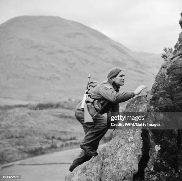 The British Army In The United Kingdom 1939-45, A soldier from No. 1 Commando, armed with a 'Tommy gun', climbs up a steep rock face during training...