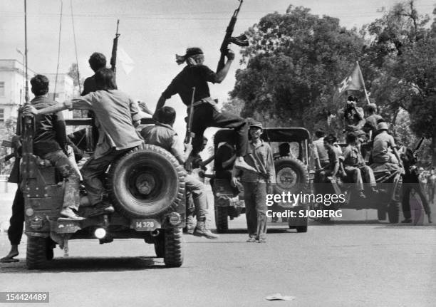 Members of the MONATIO group wearing black uniforms drive 17 April 1975 atop jeeps through a street of Phnom Penh, the day Cambodia fell under the...