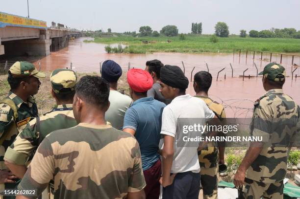 Indian Border Security Force soldiers and villagers look at the zero line fencing near India-Pakistan border submerged in floodwaters at Kartarpur...