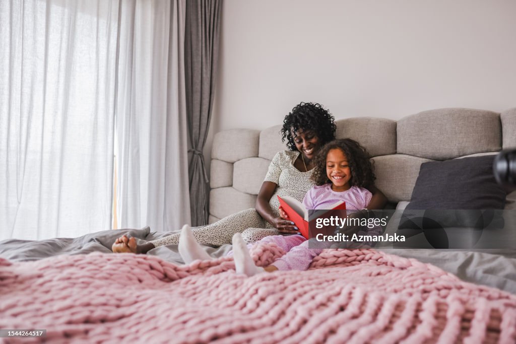 Glückliche schwarze Mutter und Tochter genießen ihre gemeinsame Zeit und lesen eine Geschichte, während sie auf einem gemütlichen Bett in einer coolen Wohnung liegen