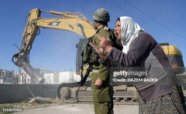 An Israeli soldier stands guard watching a bulldozer detroying the home of Mrs. Al-Jaabari, shouting, constructed near the Jewish settlement of...