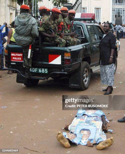 Uganda's People defence Force soldiers drive past a dead supporter of the presidential's candidate Kizza Besigye killed 15 February 2006 at the gate...