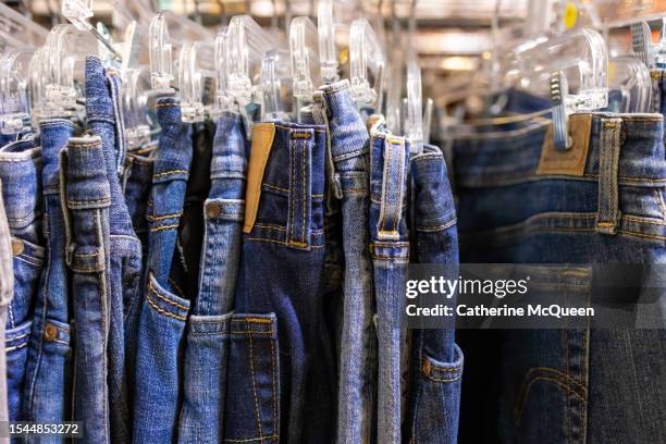 rack of vintage denim blue jeans at antique flea market - spijkerstof stockfoto's en -beelden