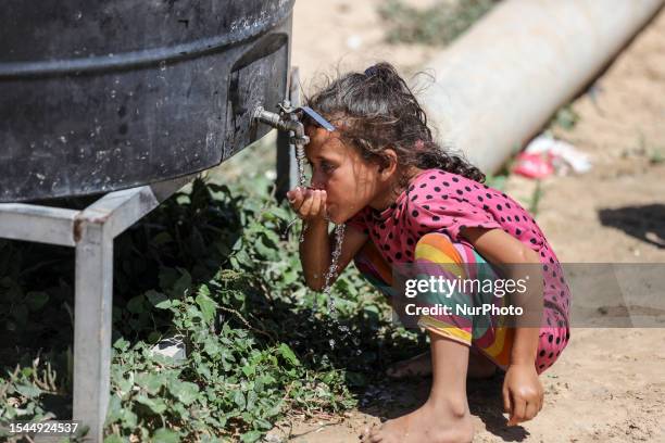 Palestinian girl drinks from a cistern next to her house during a heat wave and lengthy power cuts in Nahr al-Bared camp in Khan Yunis in the...
