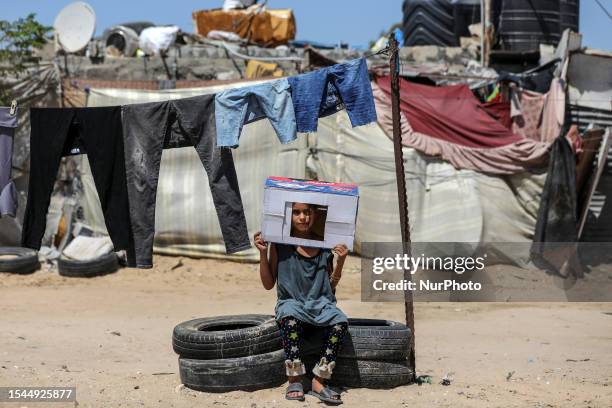 Palestinian girl sits outside her house, covering her head with a cardboard box during a heat wave and lengthy power cuts in Nahr al-Bared camp in...