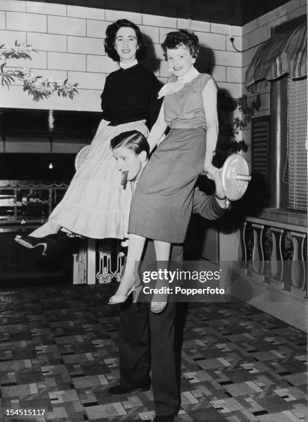 English disc jockey and manager of the Plaza Ballroom in Manchester, Jimmy Savile lifting two young women and a barbell, April 1956.