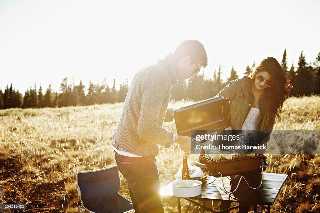 Couple cooking at barbecue in field at sunset