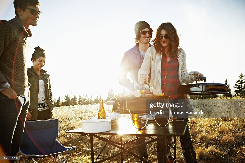 Group of friends barbecuing in field at sunset