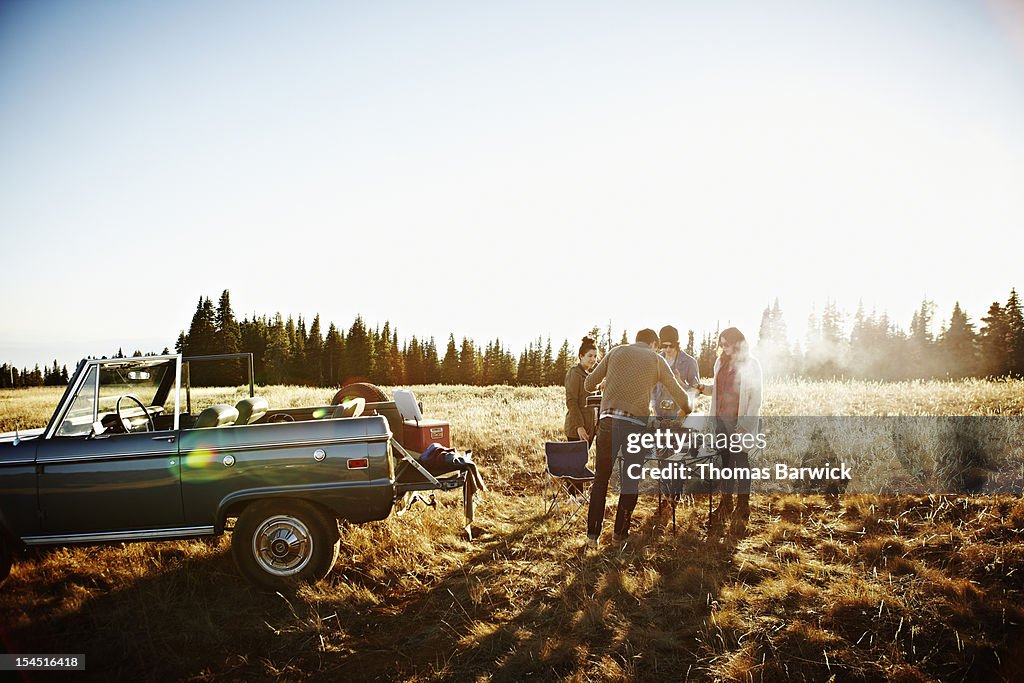 Group of friends cooking at barbecue at sunset