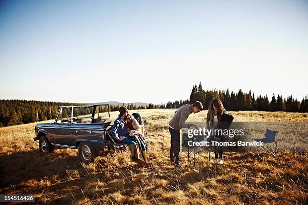 friends barbecuing in mountain top field at sunset - tailgating stock-fotos und bilder